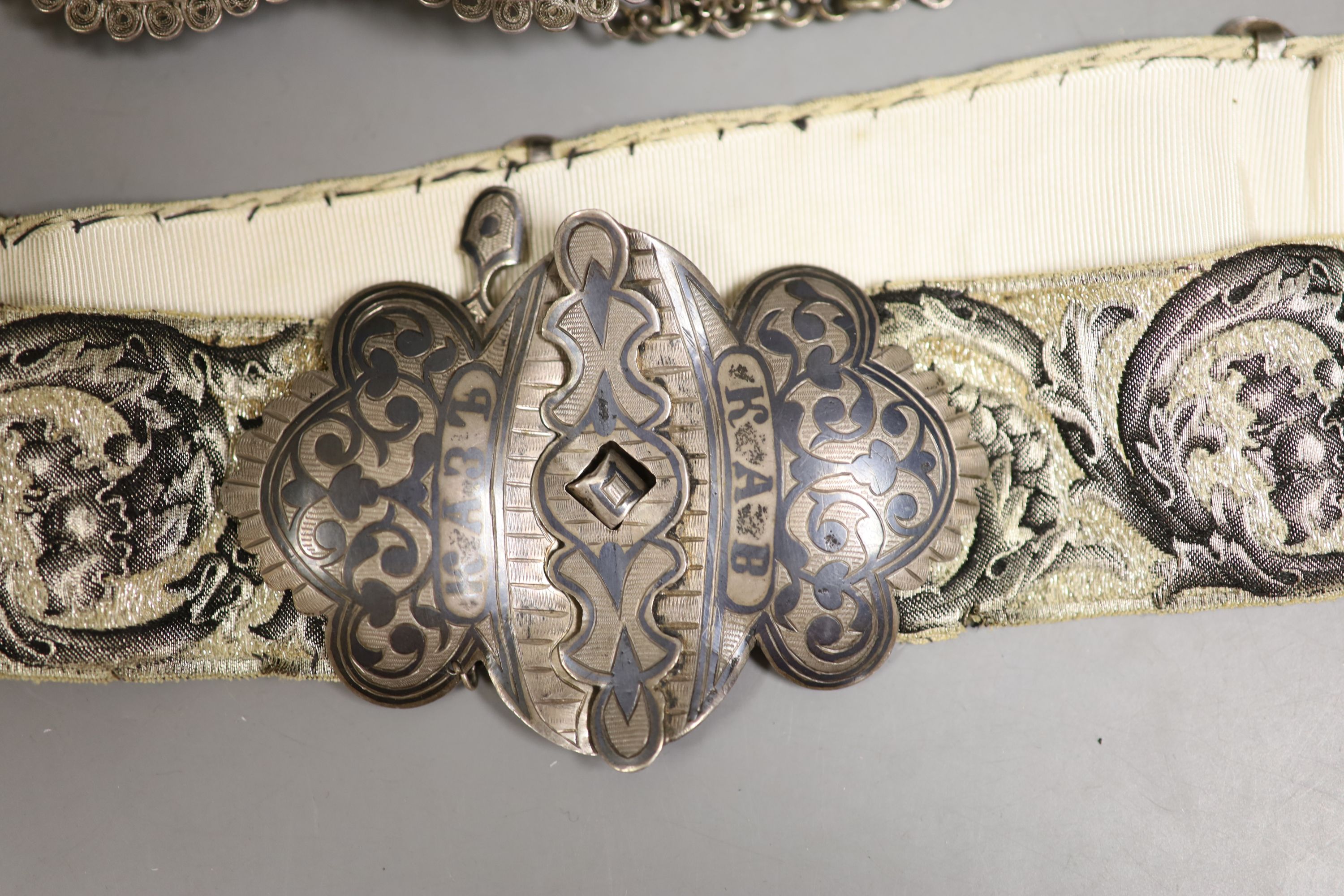 A white metal and niello belt buckle, one other on a sash belt and a filigree white metal belt.